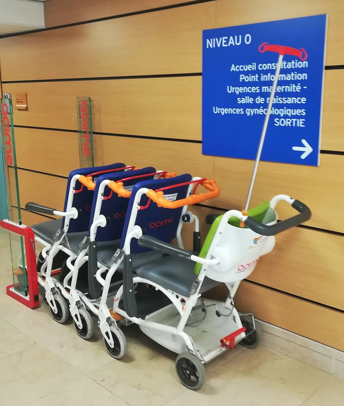 Rij vouwbare rolstoelen voor patiëntenvervoer in een ziekenhuisgang met bewegwijzering